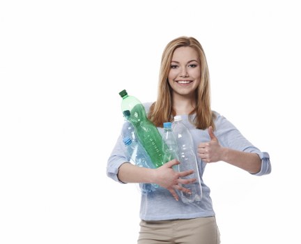 A young woman with long, straight, light brown hair and a cheerful expression is holding multiple used plastic bottles, including a green bottle and clear bottles, against a plain white background. She is wearing a light blue, long-sleeved shirt with the sleeves rolled up and appears to be giving a thumbs-up gesture with her right hand. The bottles vary in size and shape, some with labels and caps, conveying a sense of recycling or waste collection. The image is well-lit, with a focus on the bottles and her friendly demeanor, emphasizing the importance of proper rubbish disposal, such as plastic waste collection, in a manner relevant to environmental and waste management services in Raynes Park and surrounding areas.